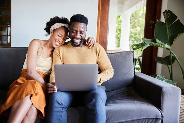 Laughing young couple using a laptop on their living room sofa